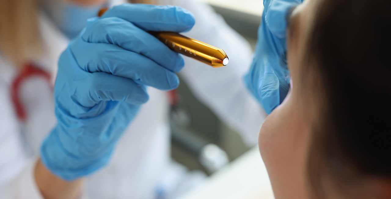 Doctor neurologist shining flashlight on patient eyes in clinic closeup
